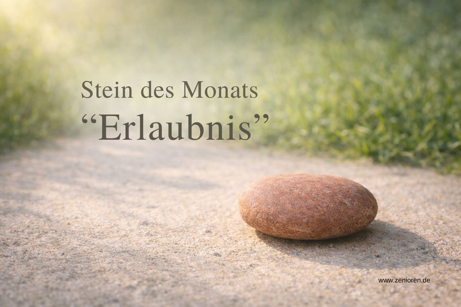 Zenioren „Stein des Monats: Erlaubnis“: Ein einzelner naturbelassener Stein in erdigem Rotton liegt im warmen Morgenlicht auf hellem Weg- oder Sandboden. Im Hintergrund weiches salbeigrünes Frühlingsgrün, klare Texturen, viel ruhiger Freiraum. Overlay-Text: „Stein des Monats – Erlaubnis“.