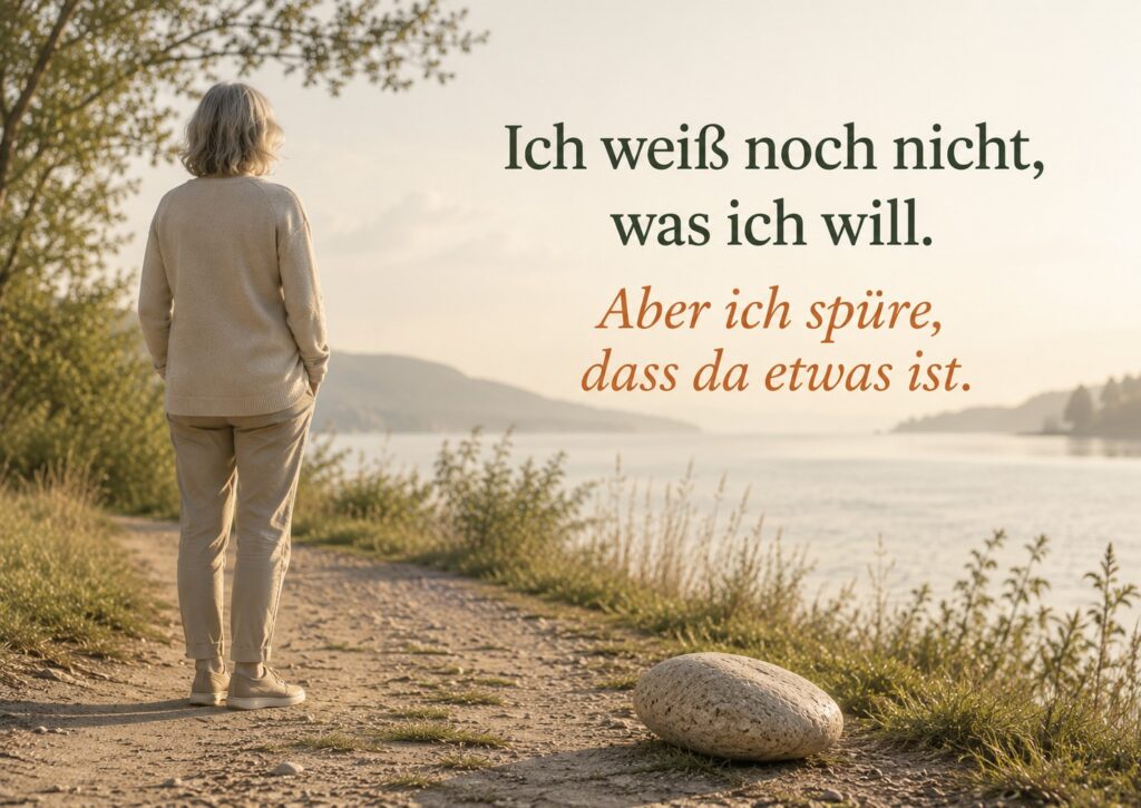 Zenioren-Bild mit einer älteren Frau von hinten auf einem ruhigen Weg am Wasser. Ein einzelner naturbelassener Stein liegt leicht außerhalb ihrer Spur und steht für einen eigenen Willen, der noch keinen klaren Namen hat, aber bereits spürbar wird. Im Bild steht: „Ich weiß noch nicht, was ich will. Aber ich spüre, dass da etwas ist.“